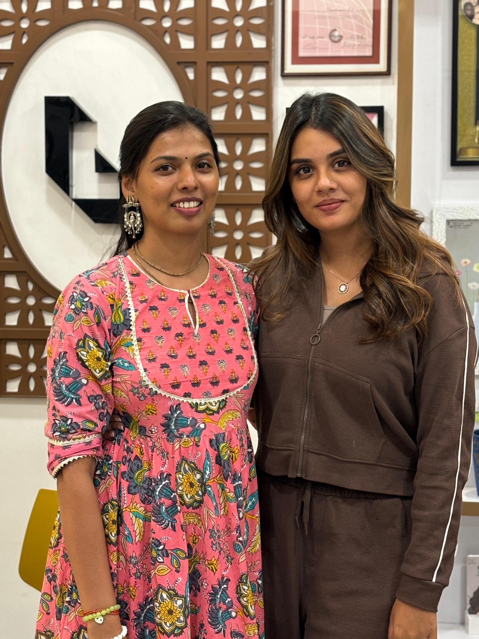 Two women posing beside the salon's decorative wall