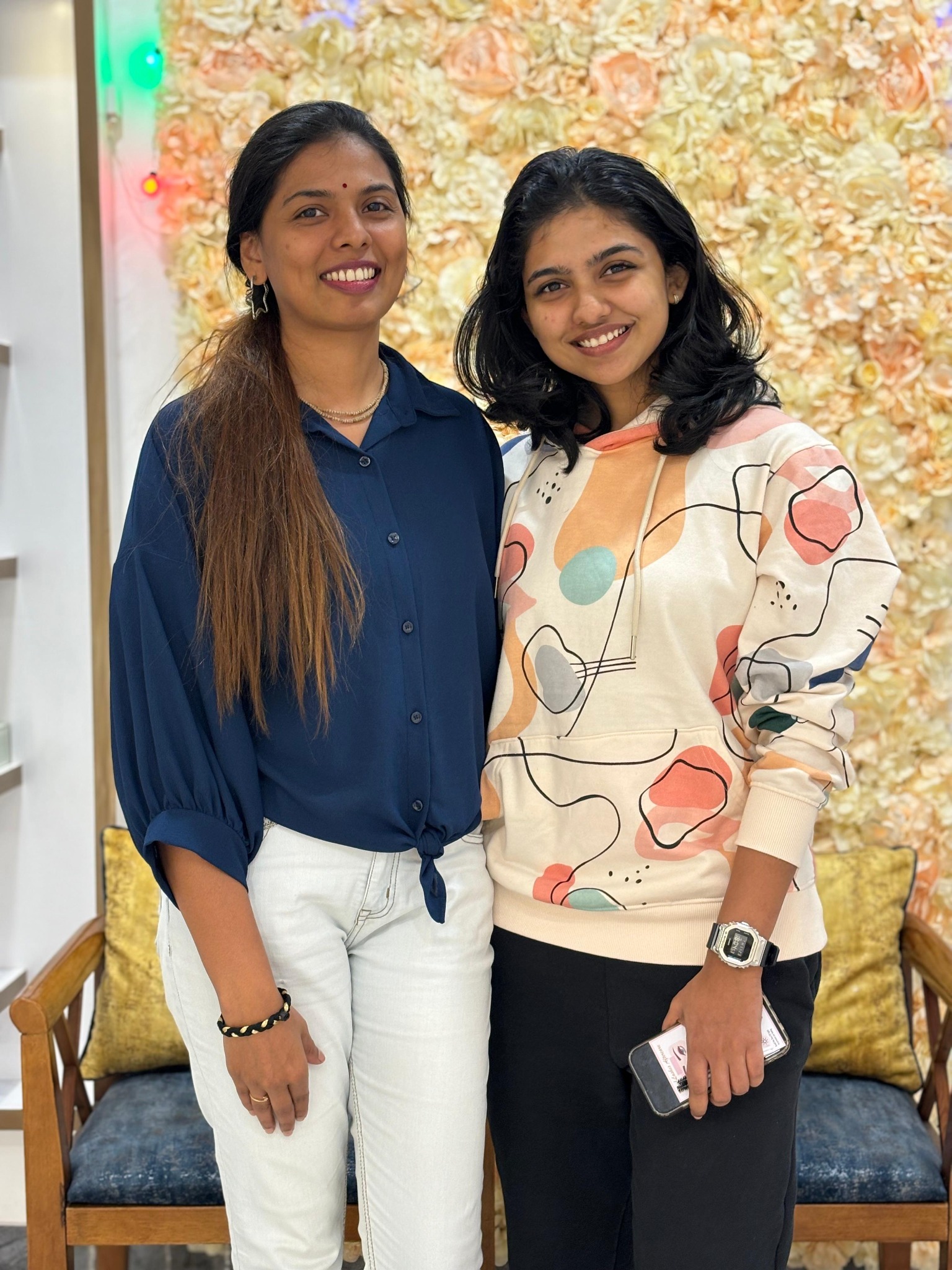 Two women smiling in front of the floral wall at Greatlooks Salon